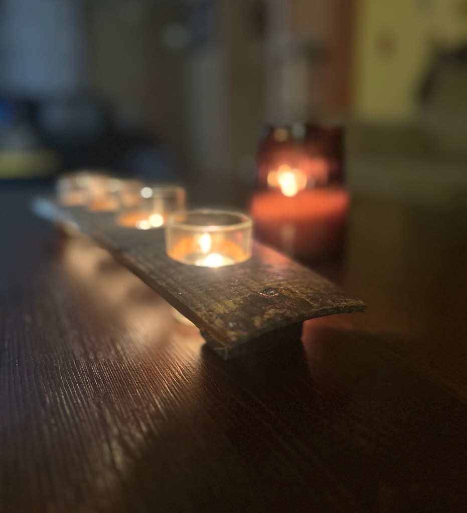 Wooden candle holder with glowing tea lights on a dark table.